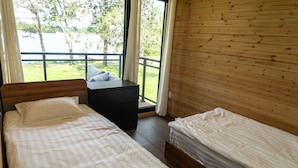 Un dormitorio con dos camas, cabecera de madera, una mesita de noche y vista a un lago a través de un ventanal grande.