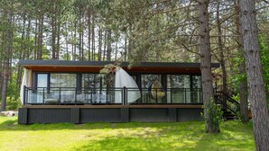 Una cabaña moderna con ventanas grandes, una terraza y una escalera que lleva a una terraza de madera.