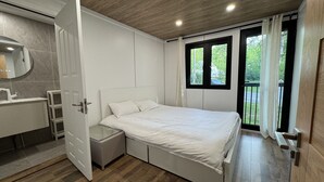 Een moderne slaapkamer met een groot bed, een inbouwkast, een badkamer met spiegel en uitzicht op groen door de ramen.