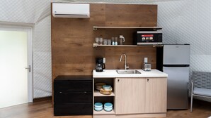 A compact kitchen with a built-in microwave, toaster, and refrigerator, a sink, and a small cabinet with dishes.