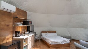 A modern, compact bedroom with a wooden bed, a small kitchenette, and a unique geometric ceiling design.