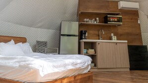 Um quarto com uma cama de madeira, um pequeno espaço de cozinha e uma janela grande.