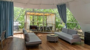 A spacious tent with a wooden floor, a sofa, a chair, and a small table.