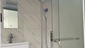 Een moderne badkamer met een douchecabine van glas, een wit toilet en een marmeren wastafel met een spiegel.