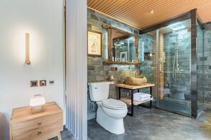 A modern bathroom with a stone wall, a wooden vanity, a toilet, and a glass shower enclosure. - Liaoshe Garden Hotel (Jianchuan)