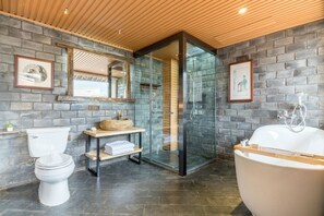 A modern bathroom with a stone wall, a wooden ceiling, a glass shower enclosure, a white toilet, a wooden vanity, and a freestanding bathtub. - Liaoshe Garden Hotel (Jianchuan)