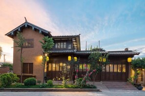 A traditional building with a sloped roof, wooden doors, and a garden with various plants. - Liaoshe Garden Hotel (Jianchuan)
