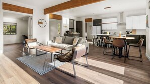 Un vaste espace de vie comprenant un canapé, une table basse et des fauteuils, une cuisine avec des meubles blancs et un coin repas avec une table et des chaises.
