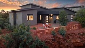 Une maison moderne avec un toit plat, de grandes fenêtres et un patio aménagé avec des chaises.