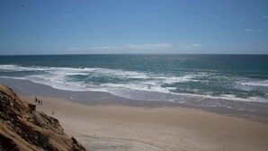 Ein Strand mit Wellen, blauem Himmel und einer felsigen Klippe.