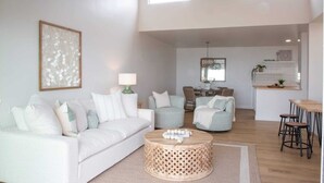 Ein modernes Wohnzimmer mit einem weißen Sofa, einem runden Couchtisch und einem Essbereich mit Barhocker.