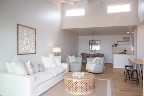 A modern living room with a white sofa, a round coffee table, and a dining area with bar stools.