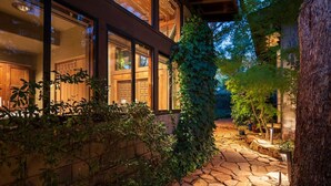 Un chemin de pierres mène à un bâtiment en bois doté de grandes fenêtres et d’un porche abrité.