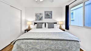 A bedroom with a bed, two wall-mounted lamps, a ceiling fan, and two wall art pieces. - Charming 1-Bedroom Home on 29th Street (Newport Beach)