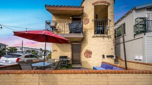 A two-story building with a balcony, outdoor seating, and a garage. - Charming 1-Bedroom Home on 29th Street (Newport Beach)
