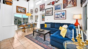 Ein großzügiger Wohnbereich mit blauem Sofa, Esstisch und Stühlen, dekoriert mit verschiedenen gerahmten Kunstwerken und einer roten Lampe.