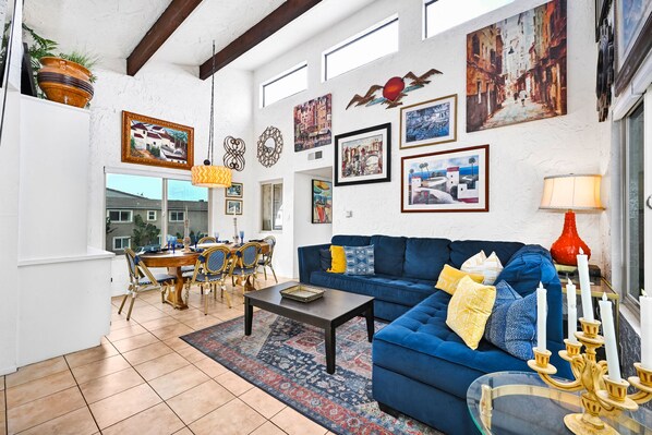 A spacious living area with a blue sofa, dining table, and chairs, decorated with various framed artworks and a red lamp.