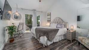 A bedroom with a large bed, a ceiling fan, a bedside table with a lamp, a chair, a potted plant, and a view of the outdoors. - Lovely 2BA King Beds+2 Car Garage. Hidden Gem-Walk>Shops & Dining! (Littleton)