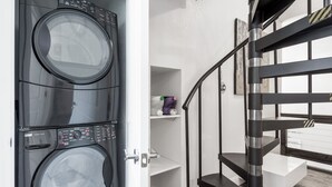 A laundry room with two stacked front-loading washing machines, a white shelving unit, and a black spiral staircase. - Lovely 2BA King Beds+2 Car Garage. Hidden Gem-Walk>Shops & Dining! (Littleton)