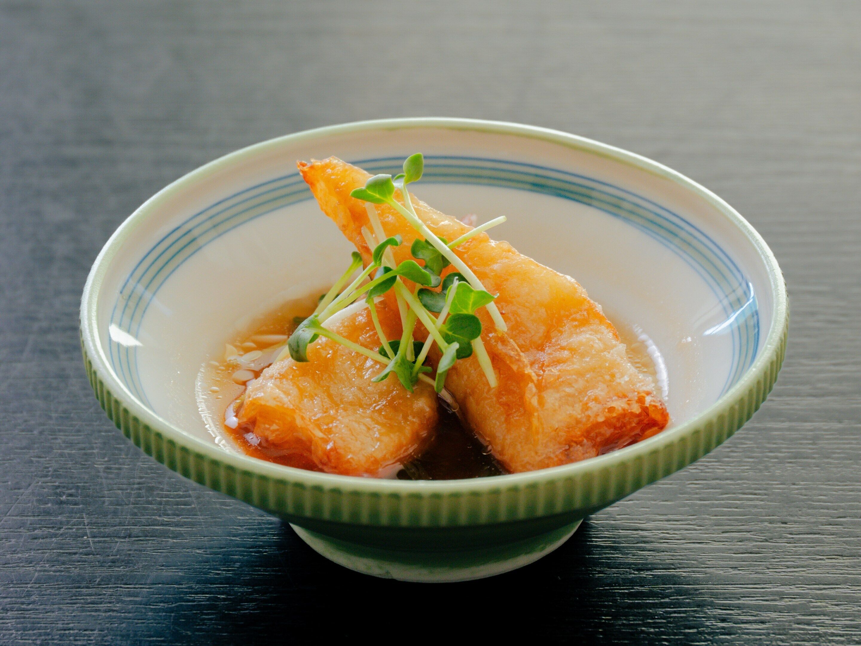 A bowl of food with a green rim on a dark surface.