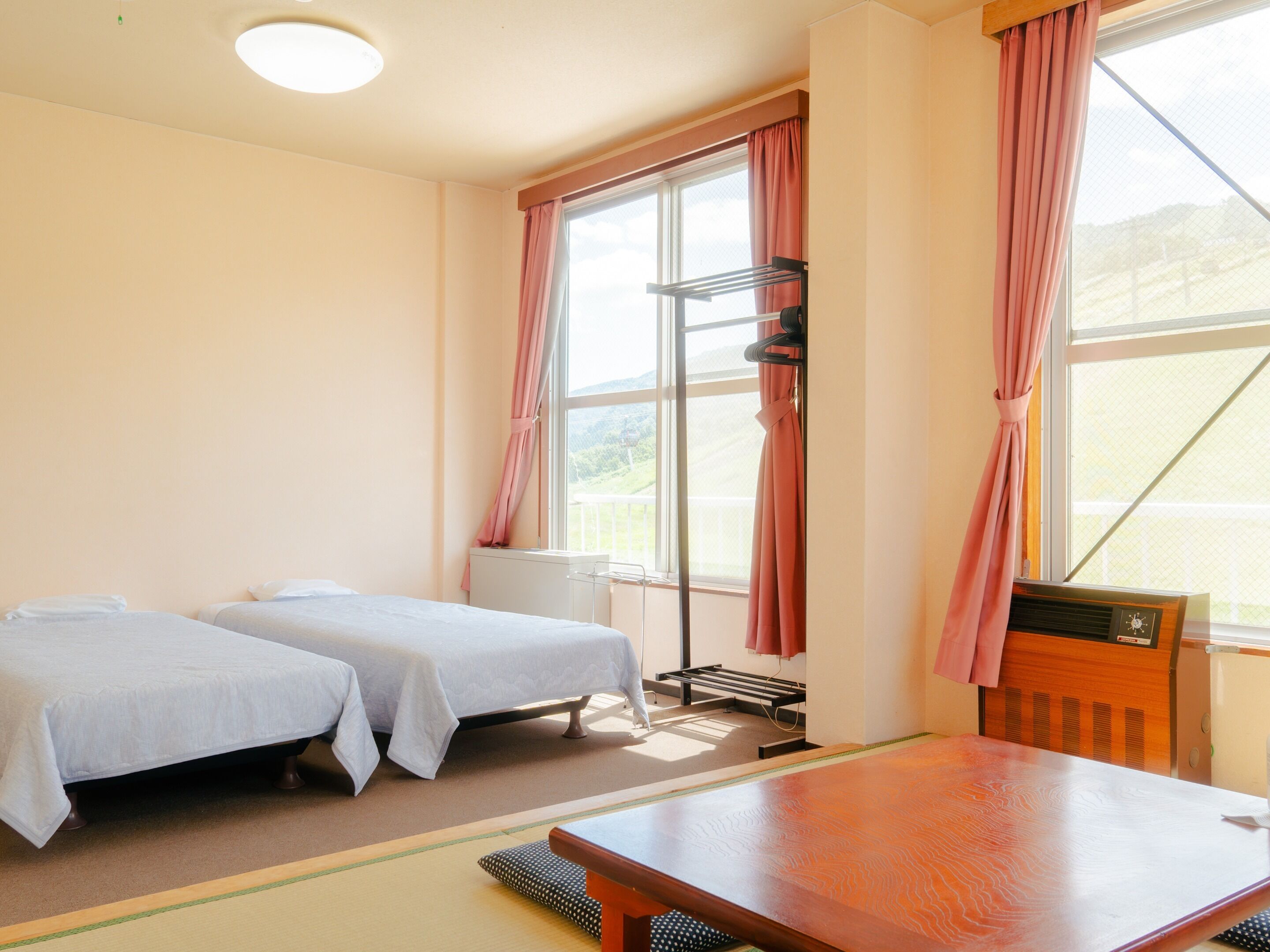 A hotel room with two beds, a wooden table, and a window with curtains.