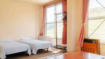 A hotel room with two beds, a wooden table, and a window with curtains.