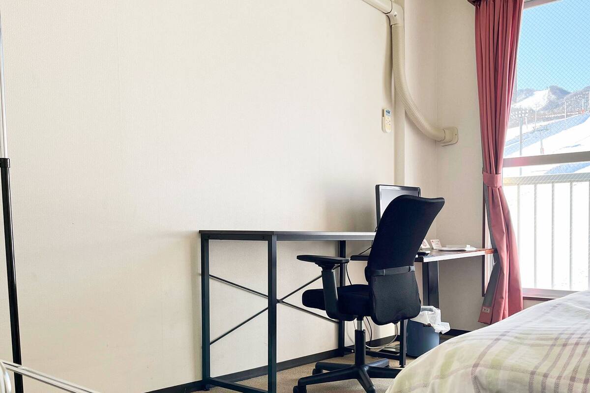 Ein Hotelzimmer mit Bett, Schreibtisch mit Computer und Fenster mit Blick auf eine verschneite Landschaft.