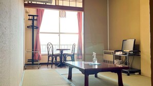 A room with a tatami mat floor, a wooden table, two chairs, a TV on a stand, and a window with pink curtains. - ishiuchiskicenter (Minamiuonuma)