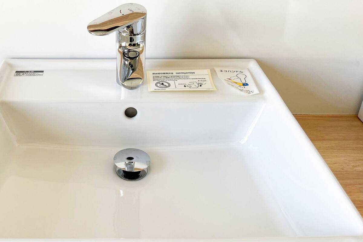 Ein weißes Waschbecken mit chromfarbenem Wasserhahn, einem Abflussstopfen und zwei Anleitungen auf der Arbeitsplatte.