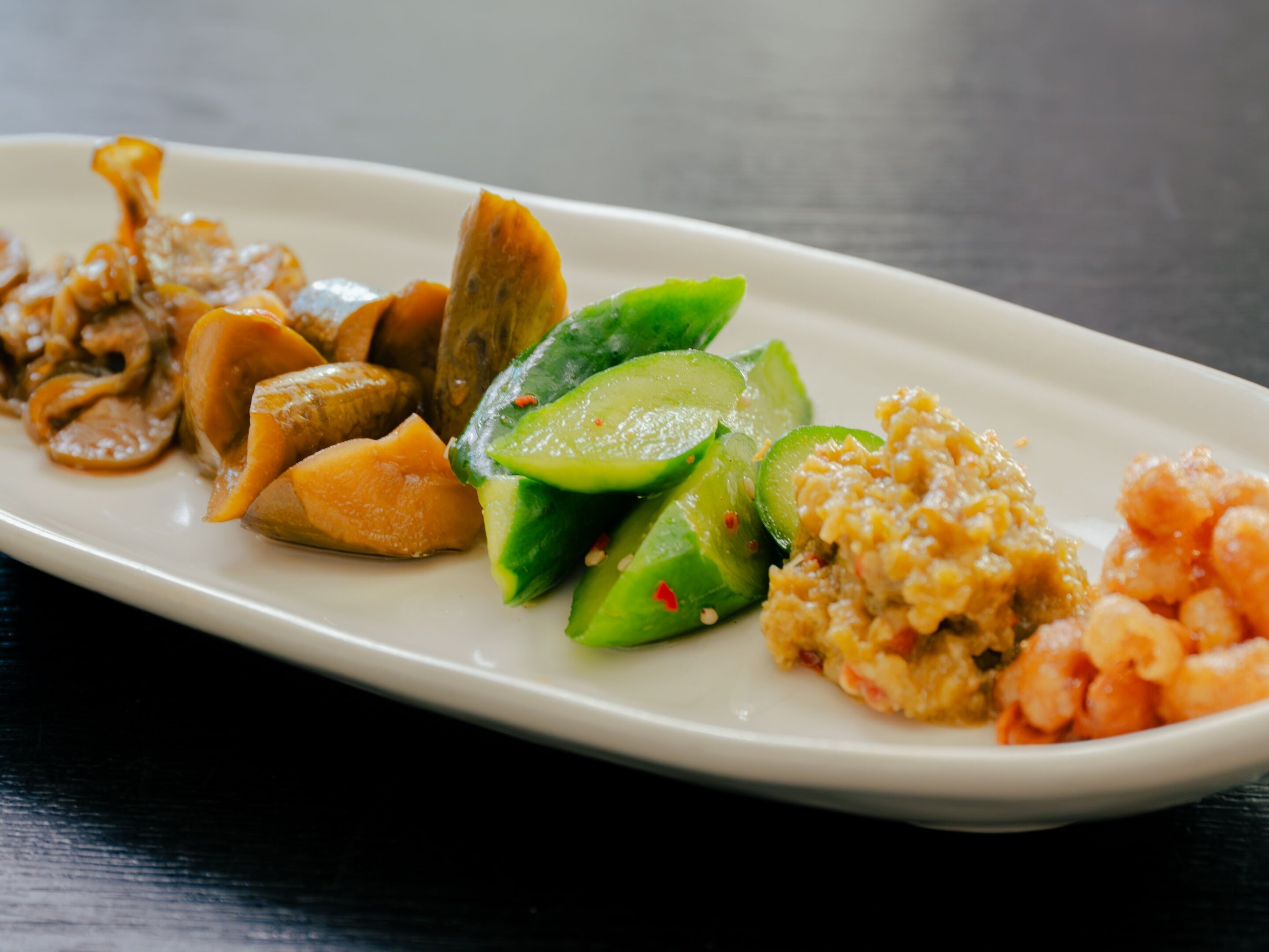 A white rectangular plate with various food items including sliced cucumbers, shrimp, and a rice dish.