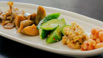 A white rectangular plate with various food items including sliced cucumbers, shrimp, and a rice dish.