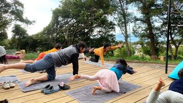 A group of people practicing yoga outdoors on a wooden deck with trees in the background.