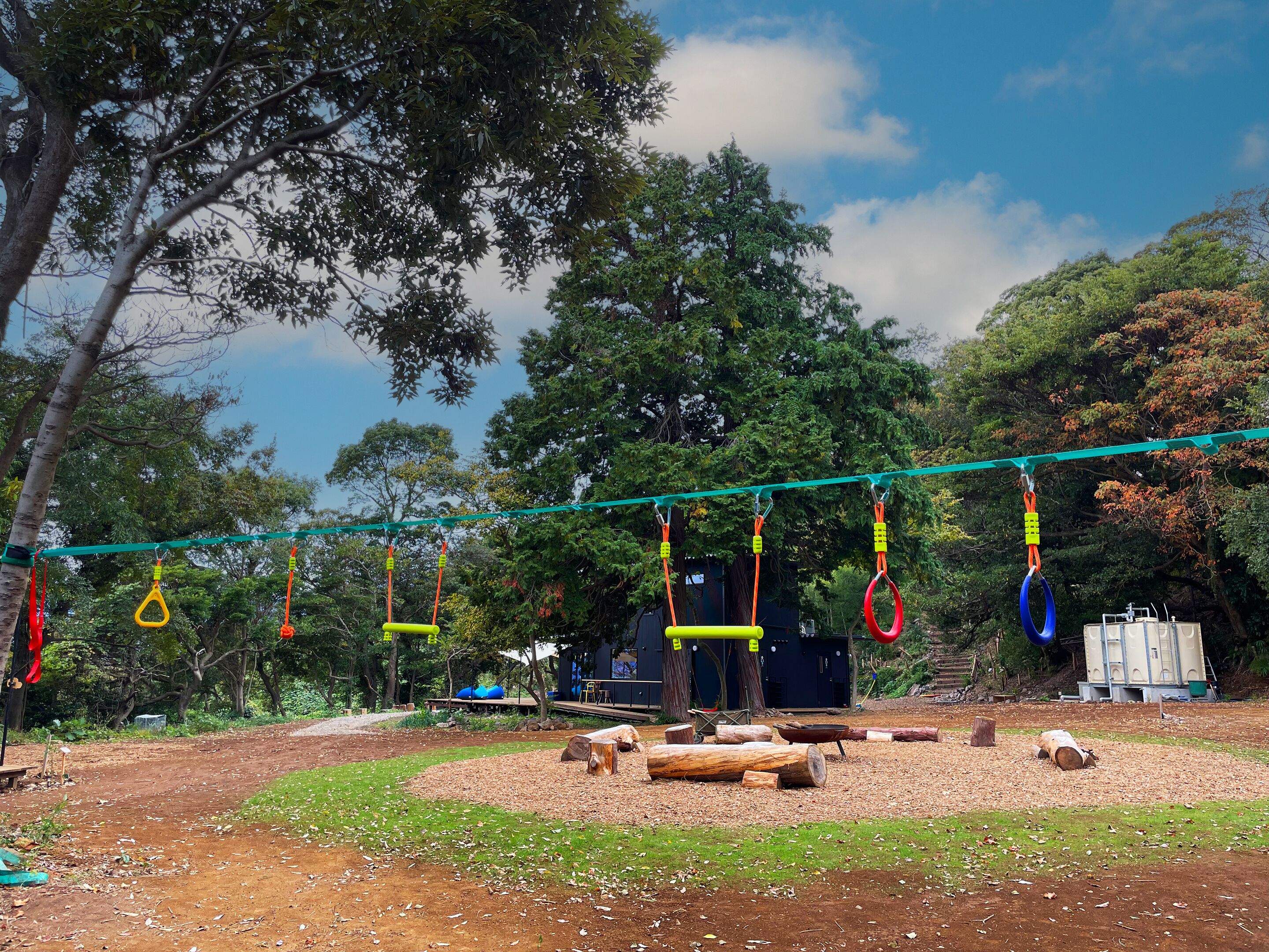 Ein Spielplatz im Freien mit einer Hängebrücke, Schaukeln und Baumstämmen.