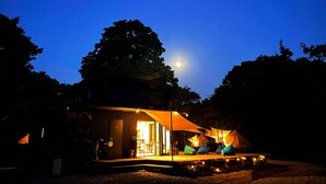 A campsite with tents and a building with a lit interior, surrounded by trees under a night sky with a visible moon. - COUSCOUS Glamping Manazuru (Manazuru)