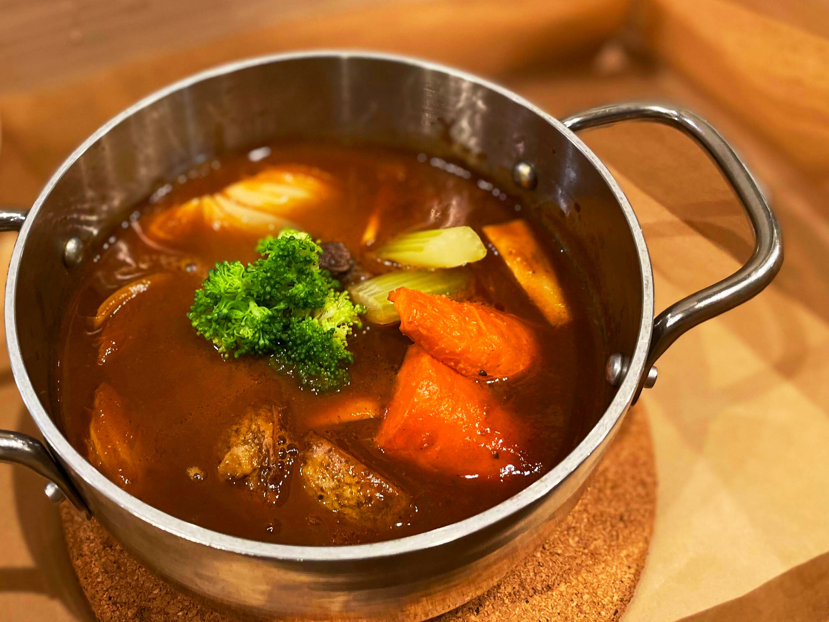 Een metalen pot met handgrepen, gevuld met een stoofpot met groenten en vlees.
