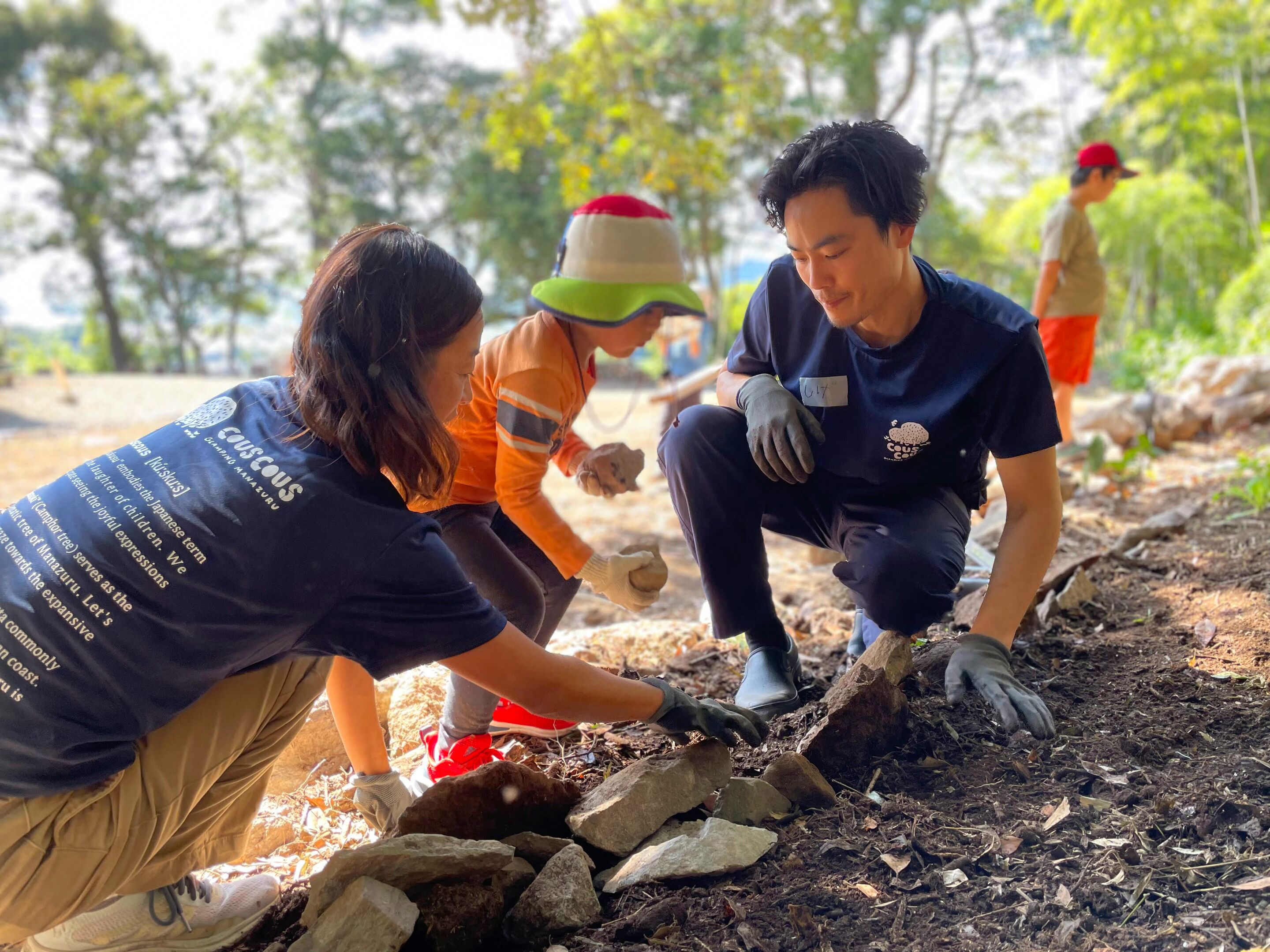 A group of people engaged in an outdoor activity, possibly a community service or environmental cleanup, in a natural setting with trees and sunlight.