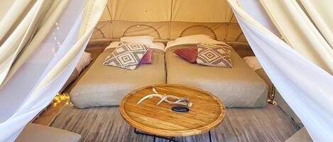 A tented accommodation with two beds, a round wooden table, and a pair of chairs.