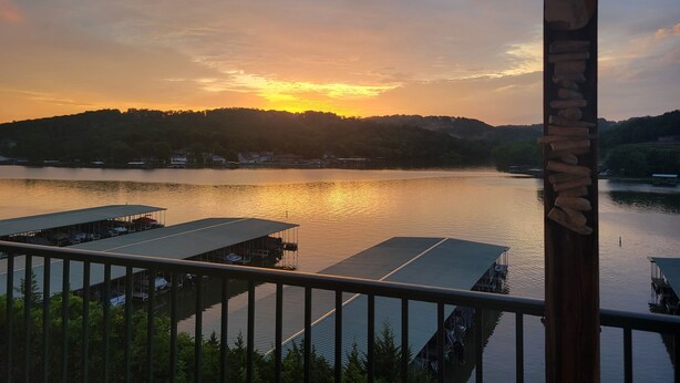 Blick auf einen See mit angestaubten Booten, einem Holzaushand und einem Sonnenuntergang.