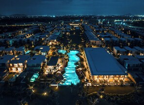 An aerial view of a resort with multiple swimming pools, connected by walkways, surrounded by well-lit villas and a large building with a pool area. - The Ocean Resort by Fusion Quy Nhon (Ngo May)