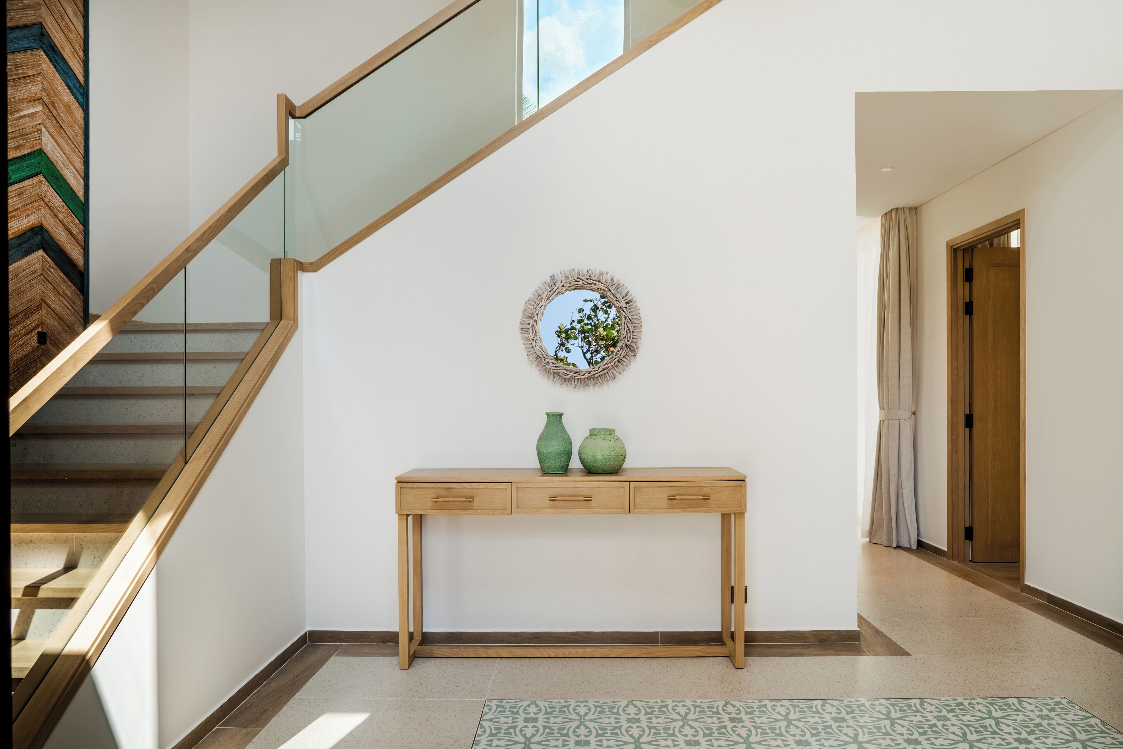 A staircase with wooden railings, a console table with two green vases, a wall-mounted mirror, and a patterned rug.