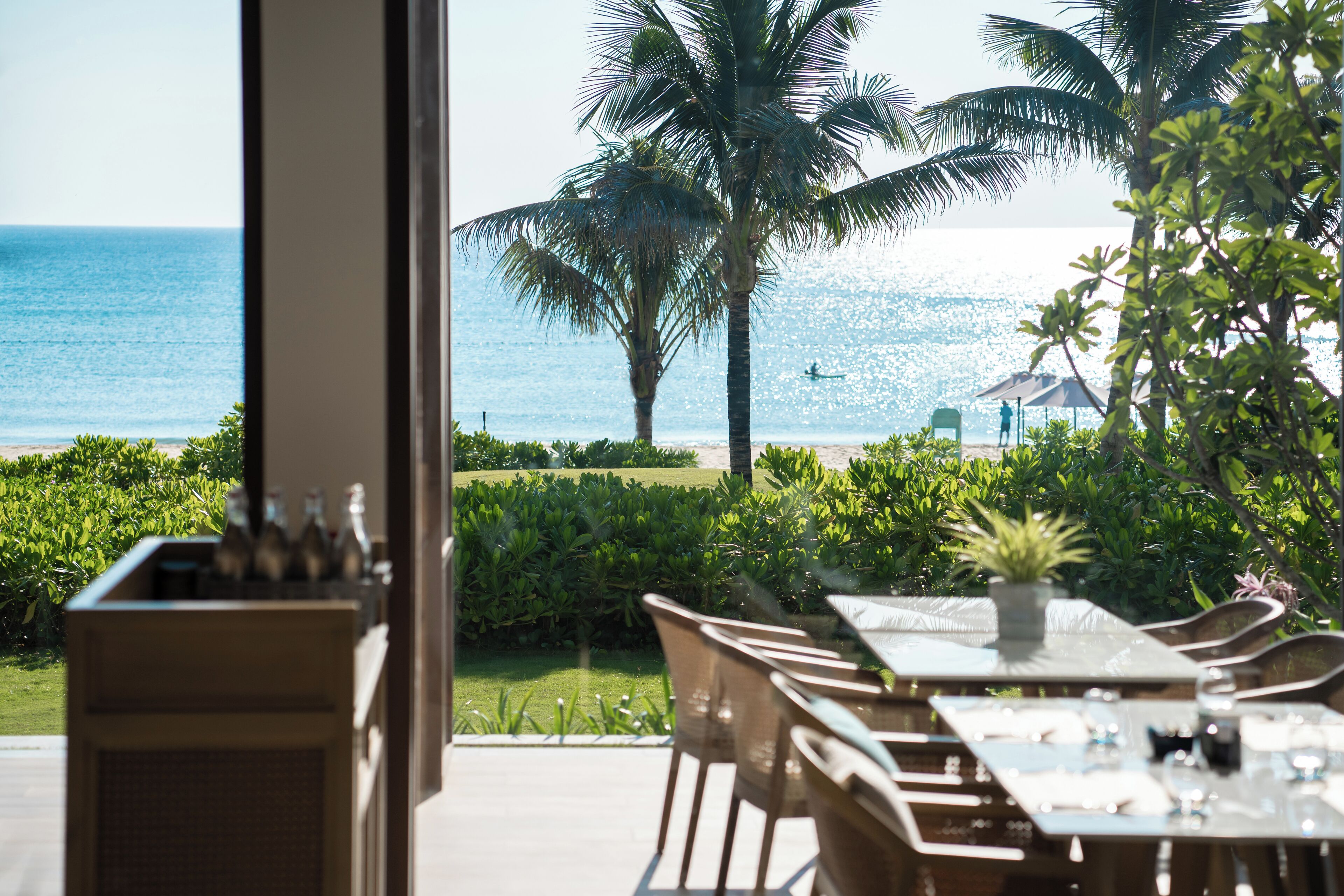 An outdoor dining area with a view of the ocean and palm trees.