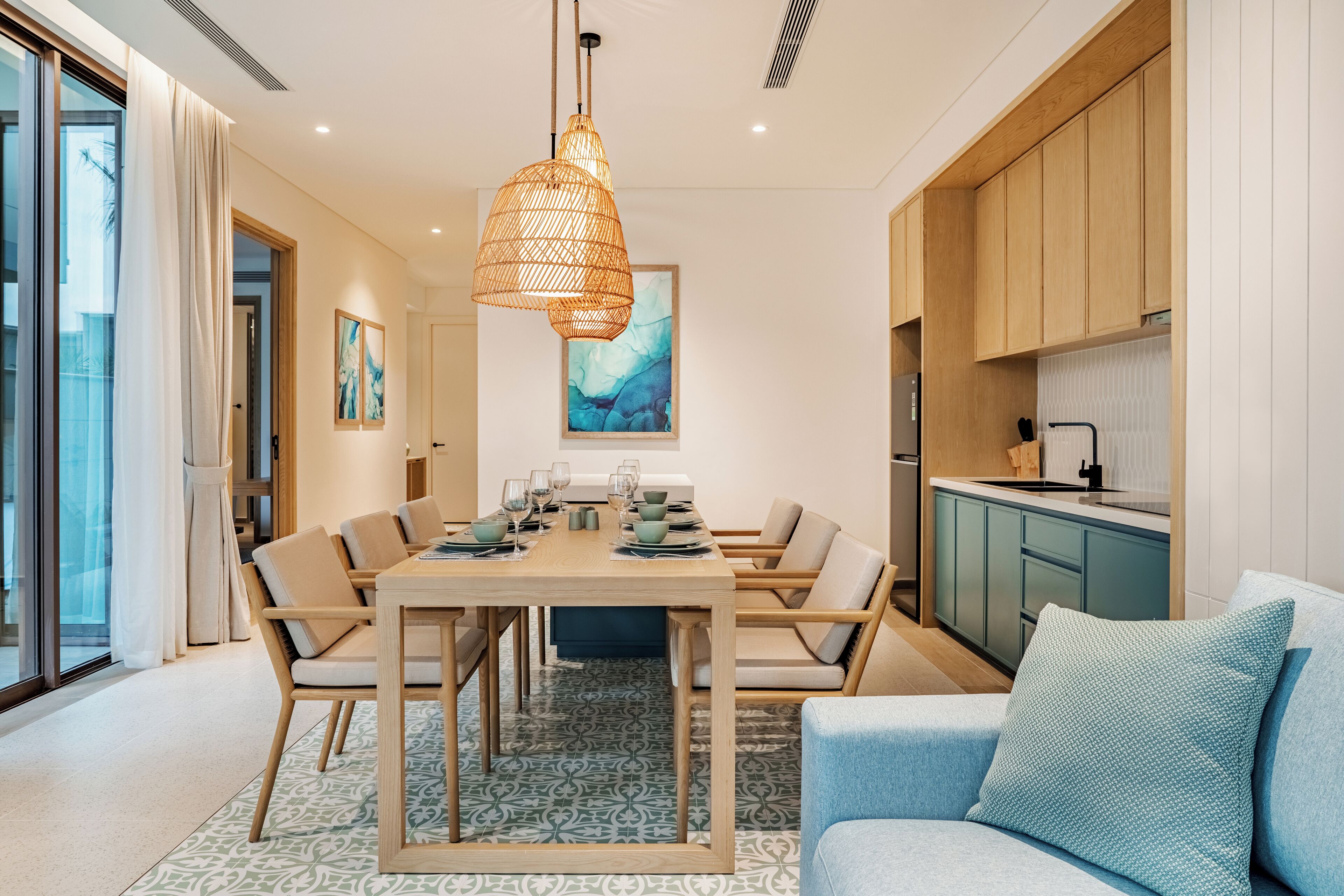Un comedor moderno con una mesa de madera dispuesta para seis personas, una lámpara colgante y vistas a la cocina.
