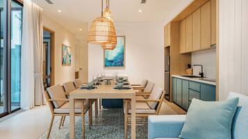Un comedor moderno con una mesa de madera dispuesta para seis personas, una lámpara colgante y vistas a la cocina.