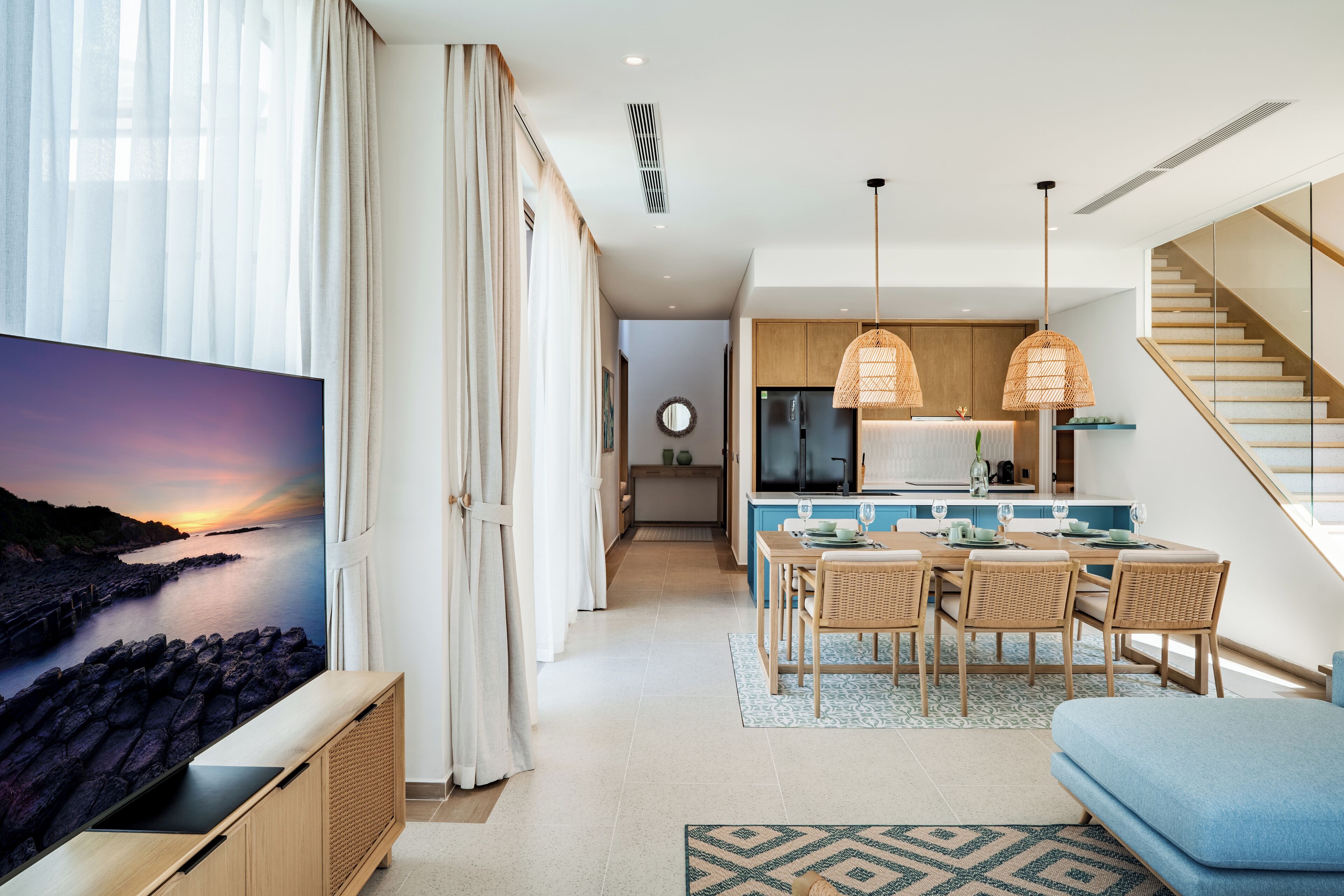 A modern living room with a TV, dining area, kitchen, and staircase.