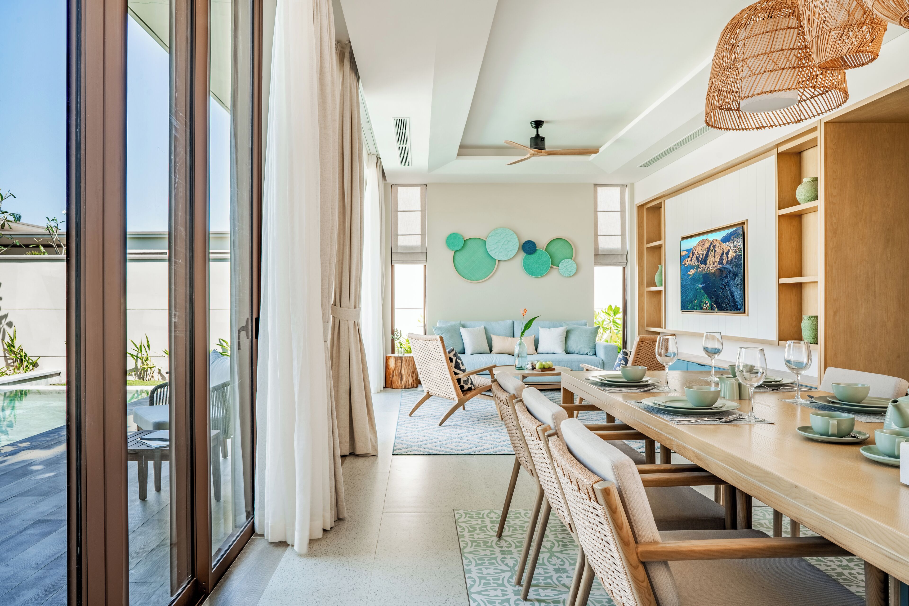 A modern dining area with a long wooden table, chairs, and a view of a pool through large sliding glass doors.
