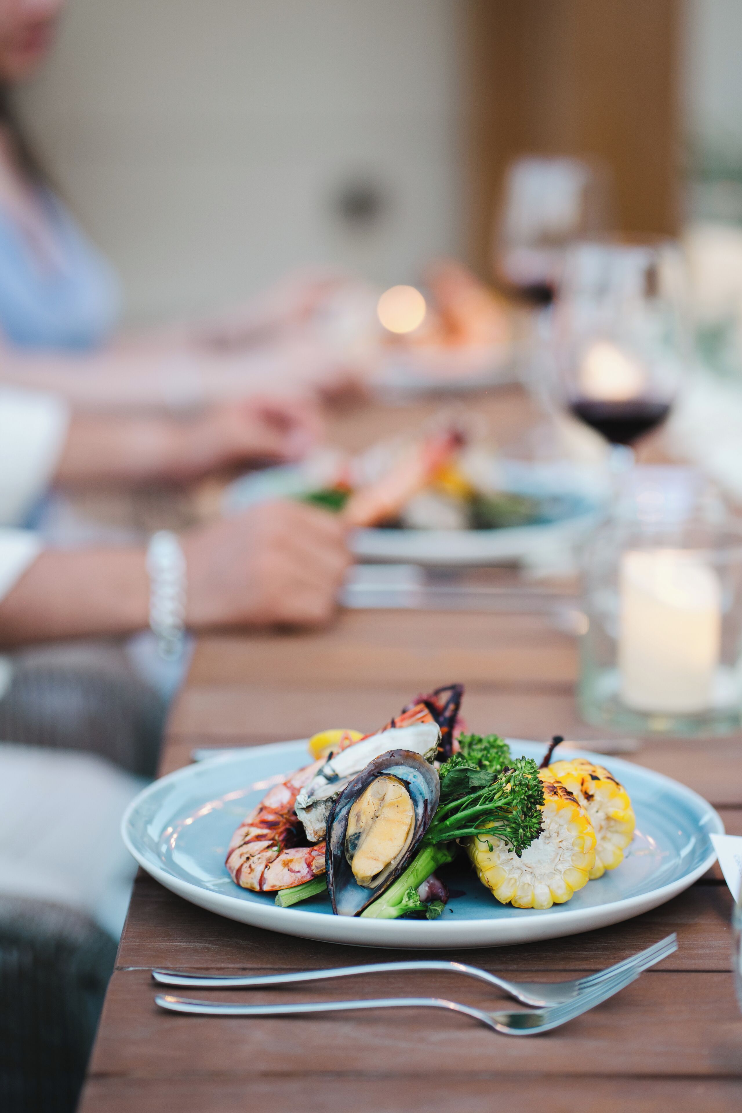 Een eettafel met borden eten, waaronder garnalen, mosselen, broccoli en maïs.