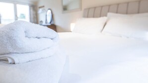 Ein ordentlich bezogenes Bett mit weißen Leinen und einem gefalteten weißen Handtuch daneben.