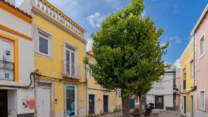 A narrow street with buildings painted in yellow and pink, a tree in the center, and a motorcycle parked on the right. - Downtown Setúbal Apartment (Setúbal)