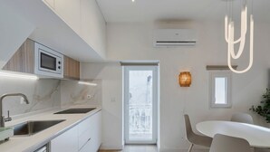 A modern kitchen with a built-in microwave, stainless steel sink, and white cabinetry. There is a dining area with a white table and chairs, and a window providing natural light. - Downtown Setúbal Apartment (Setúbal)