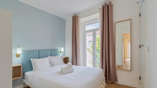 A hotel room with a bed, nightstands, a window with curtains, and a mirror. - Downtown Setúbal Apartment (Setúbal)